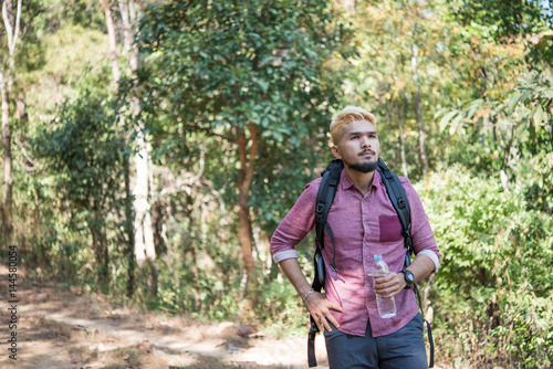 Happy hipster man tourist with backpack drinking water while hiking in nature forest. © Johnstocker