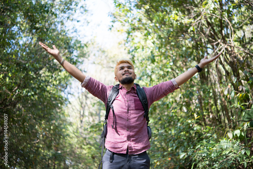 Active young man hiker open arms enjoy with nature while walking though the forest .