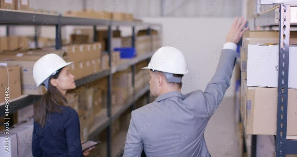 Business man & woman in discussion as they walk through industrial warehouse. Business man & woman in discussion as they walk through industrial warehouse.