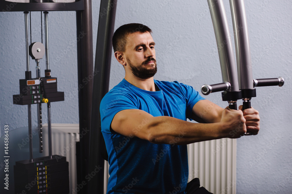muscular, attractive man trains his torso muscles , doing exercises on a butterfly machine with weights, at gym. muscular, attractive man trains his torso muscles , doing exercises on a butterfly machine with weights, at gym.