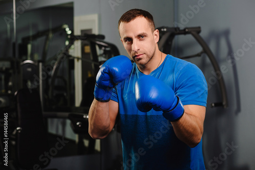 Muscular man boxer, standing in protective boxing rack and looking at camera. box training at the gym.