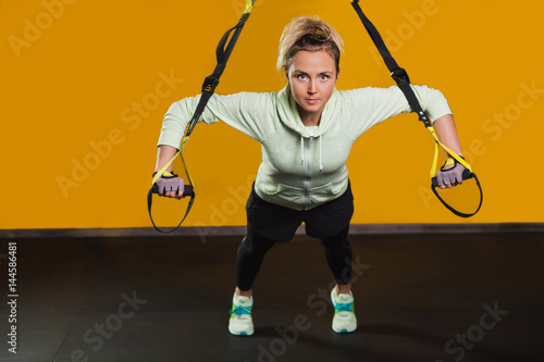 Sporty woman doing hand exercises with suspension straps Looking at camera, at gym. Suspension training for hardy body photo