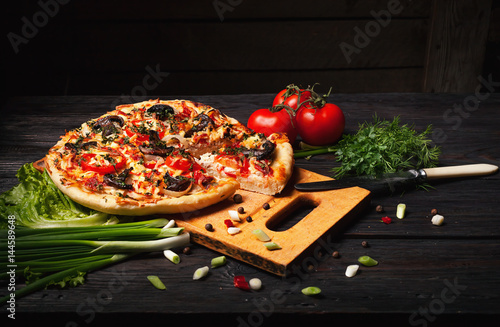 Fresh tasty pizza on black background on rustic wooden table with ingredients. Italian food.