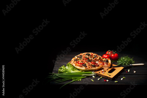 Fresh tasty pizza on black background on rustic wooden table with ingredients. Italian food.