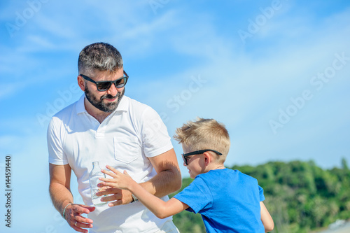 Portrait of father  teasing and not giving water to his thirsty handsome son on the desert tropical beach
