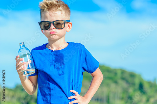 Portrait of a thirsty handsome boy in sunglasses drinking water on the desert tropical beach