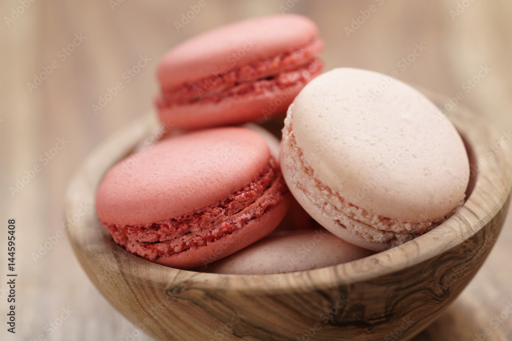 Obraz premium pastel colored macarons with strawberry and rose flavour in wood bowl on table