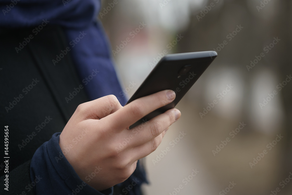 female teen hand using smartphone outddor on empty town street in spring morning, closeup photo