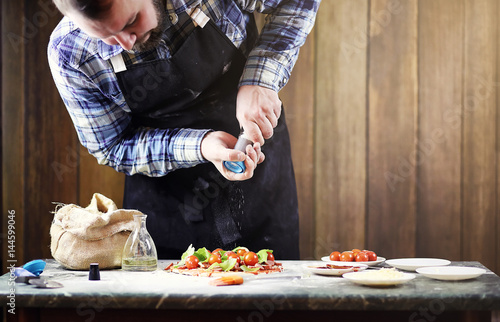 man in an apron preparing a pizza, knead the dough and puts ingr photo