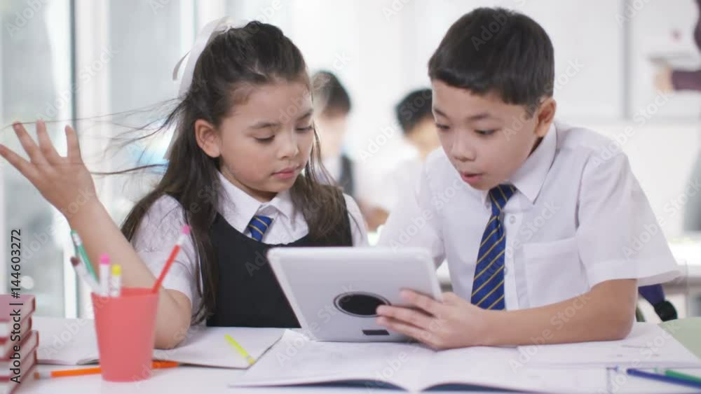Happy little boy & girl looking at computer tablet in school classroom Happy little boy & girl looking at computer tablet in school classroom