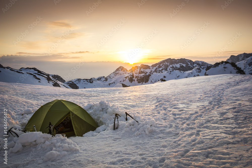 Mountaineering tent in the winter landscape surrounded by the mountain peaks at the sunset