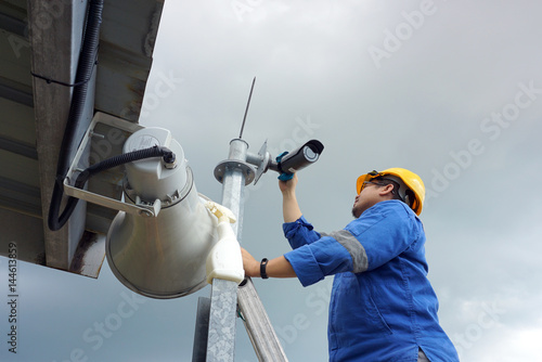 A male worker doing a maintenance work by cleaning and inspecting security camera.