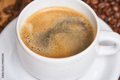 Fresh cup of coffee surrounded by coffee beans on a wooden background