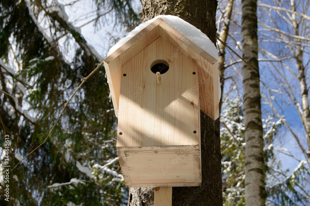 Wooden birdhouse for birds in a tree. Handmade Feeder for bird in winter forest. Caring for wild animals in difficult season.