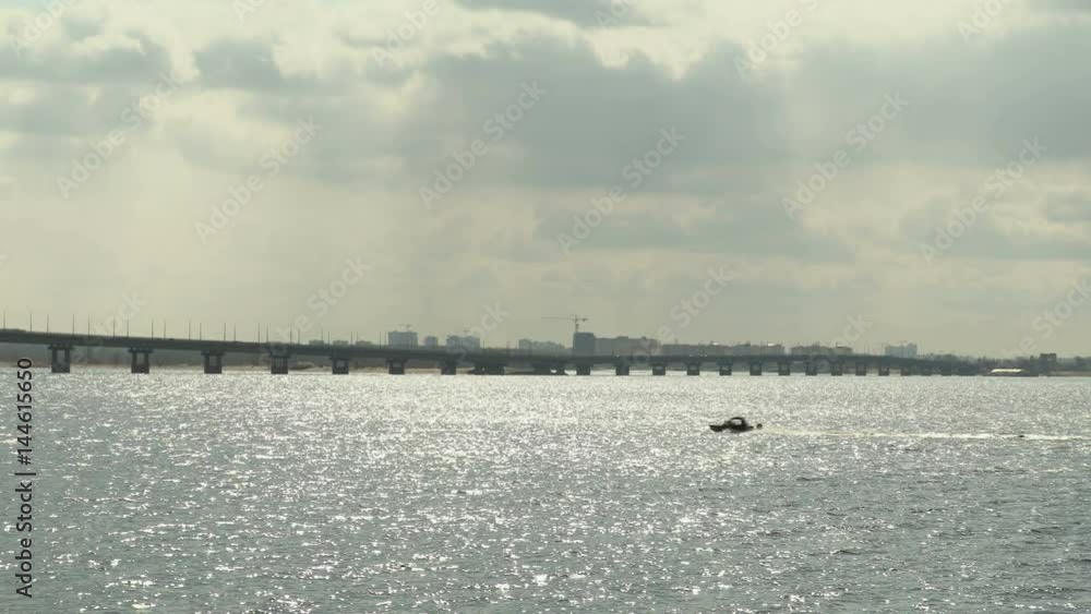 Road bridge over the Volga river between the cities of Saratov and Engels, Russia. Landscape with a river, clouds in the sky. Motor boat. 4K, Ultra HD, UHD Road bridge over the Volga river between the cities of Saratov and Engels, Russia. Landscape with a river, clouds in the sky. Motor boat. 4K, Ultra HD, UHD