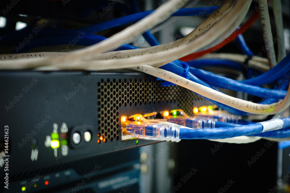 Close up of network internet cables, patch cords connected to black switch router in data center glowing in the dark and cold tone Close up of network internet cables, patch cords connected to black switch router in data center glowing in the dark and cold tone