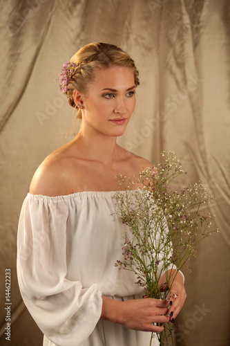 Eine Frau im weißen Kleid vor goldenem Hintergrund mit Wiesenkraut in der Hand photo