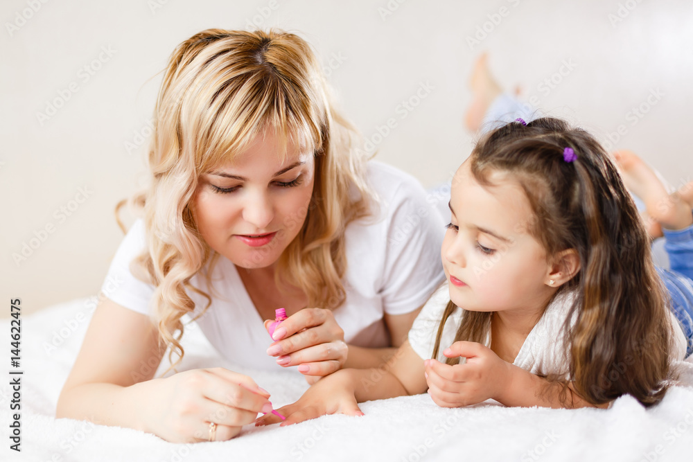 Mom and daughter in the bedroom on the bed in the curlers make up, paint their nails and have fun Mom and daughter in the bedroom on the bed in the curlers make up, paint their nails and have fun