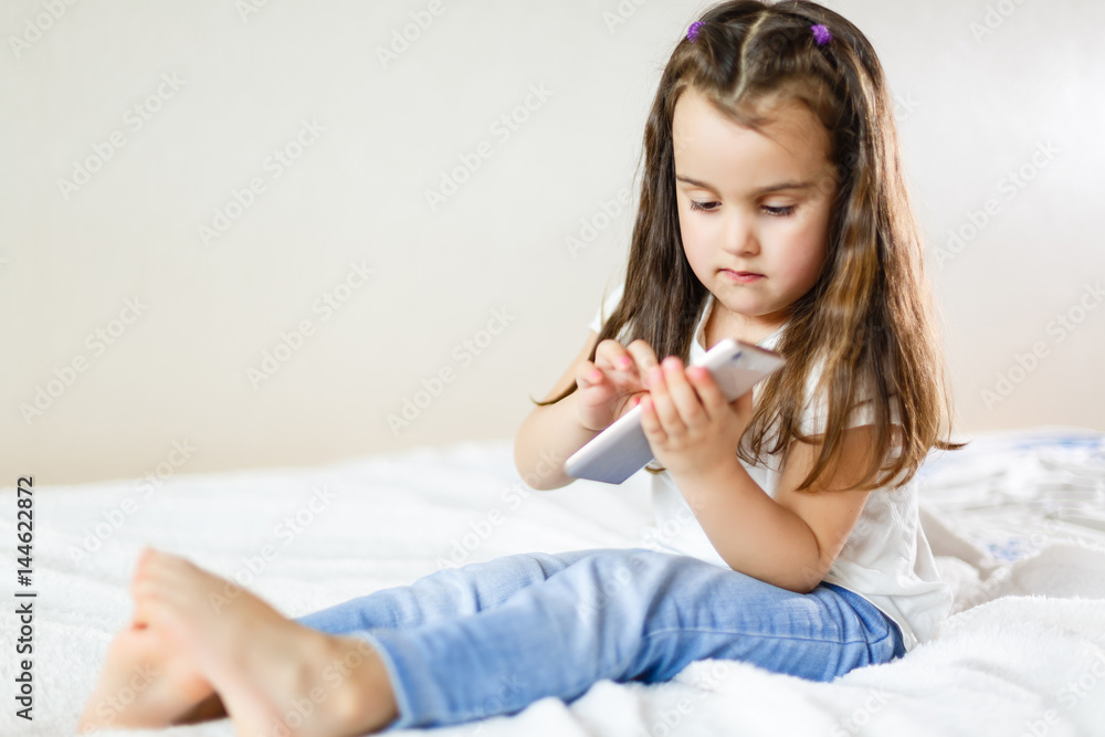 Blond kid girl playing fun with mobile smartphone on white sofa byod Blond kid girl playing fun with mobile smartphone on white sofa byod