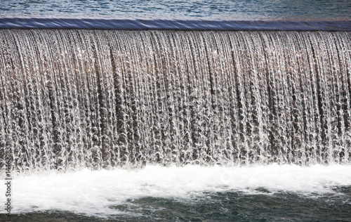 Close up of calm flowing water of a small waterfall cascading over a lip and splashing down churning up foam photo