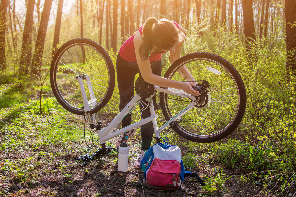 Obraz premium Young woman repairing a bicycle in the forest