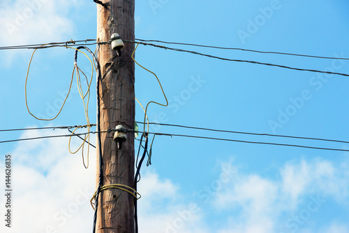 Old wooden pillar with power line against the blue sky. A botched electrical connections