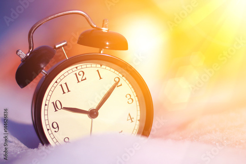 Old fashioned alarm clock in the snow with morning sunlight close up