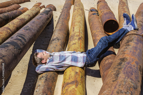 Fotografija Young man dozed off, lying on metal pipes