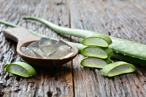 aloe gel on wooden spoon with aloe sliced on wooden table. photo