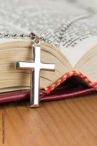Necklace with silver cross on wooden table and opened bible book