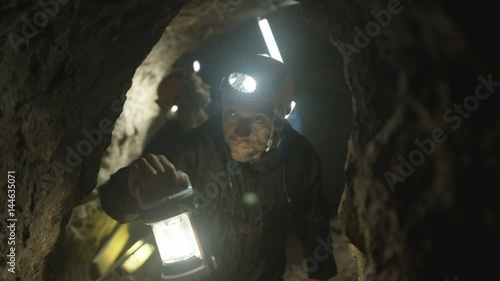  Team of potholers with hard hats and lamps exploring underground cave system