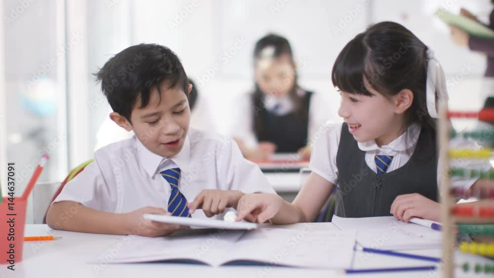 Happy little boy & girl looking at computer tablet in school classroom Happy little boy & girl looking at computer tablet in school classroom