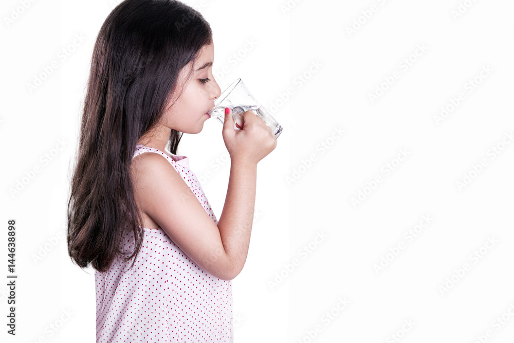 Beautiful happy little girl with long dark hair and dress holding glass of water. side view and drink water with closed eyes. studio shot, isolated on white background.. Beautiful happy little girl with long dark hair and dress holding glass of water. side view and drink water with closed eyes. studio shot, isolated on white background..