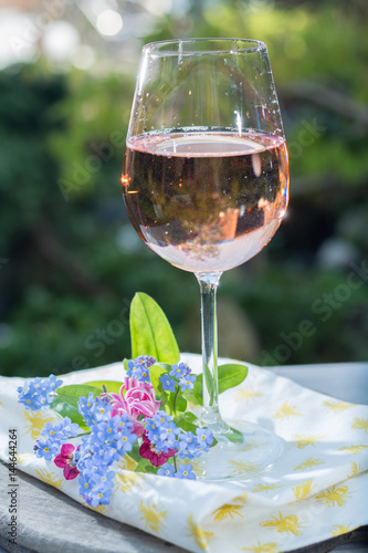Glass of cold rose wine, outdoor terraсe, sunny day, spring garden flowers