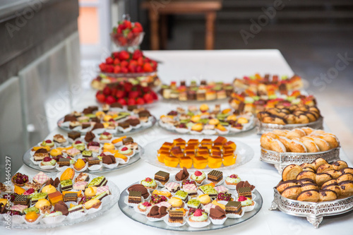 Rows of tasty looking desserts in beautiful arrangements. Mini desserts on catering buffet white tablecloth. Sweets on banquet table - picture taken during catering event
