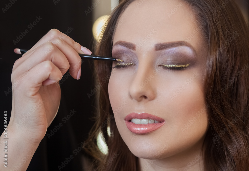 The make-up artist paints eyes with eye shadow in the beauty salon.