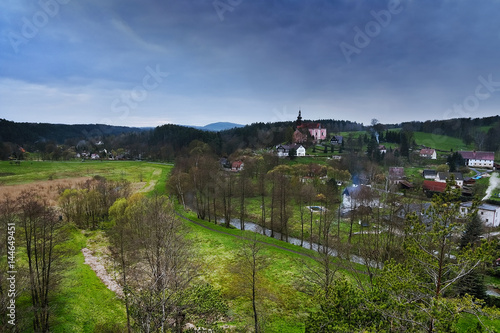 Srbska Kamenice, Czech republic - April 08, 2017: river Kamenice flowing through village with a church on hill in spring natural reserve Arba in tourist area Labske piskovce at evening