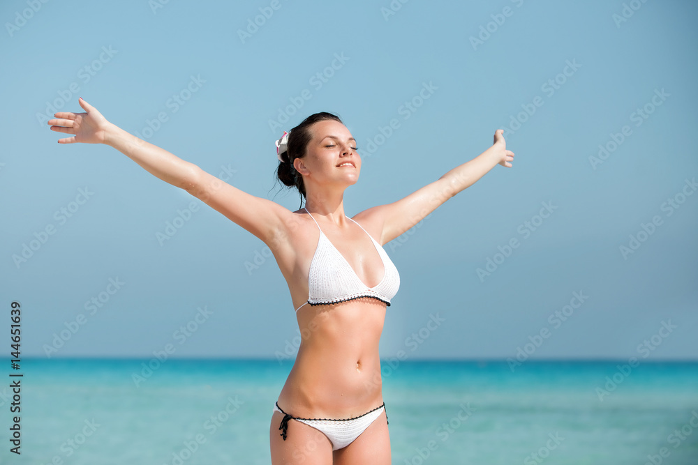Young woman with raised hands standing on the shore. Female on the beach with her hands outstretched. Young woman with raised hands standing on the shore. Female on the beach with her hands outstretched.