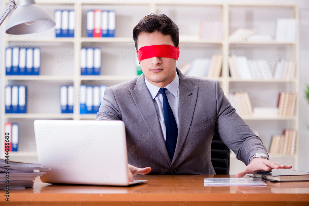 Blindfold businessman sitting at desk in office Blindfold businessman sitting at desk in office