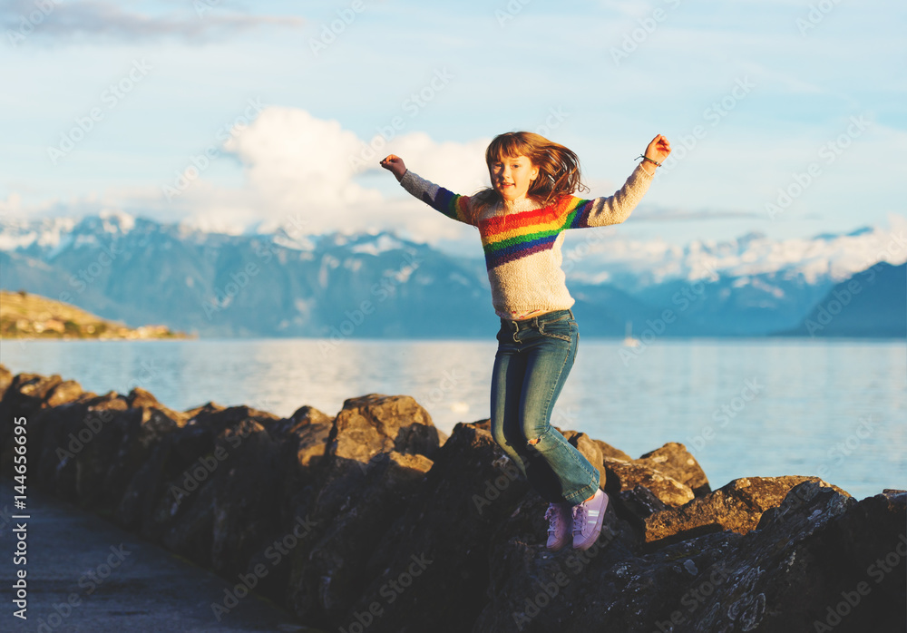 Happy and young kid girl playing next to lake geneva at sunset, arms wide open