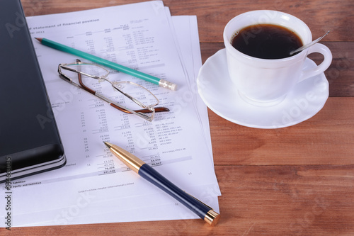 A Cup with coffee, notebook, pen and glasses on the desktop
