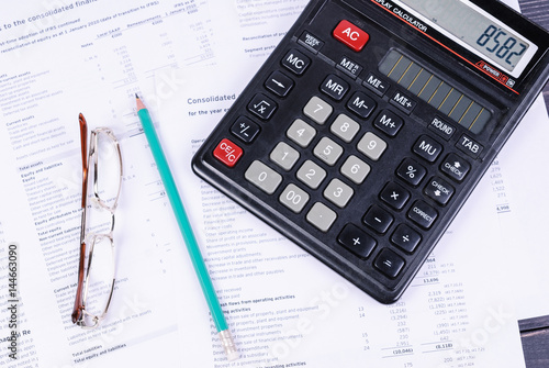 Glasses, pencil and calculator lying on reports.