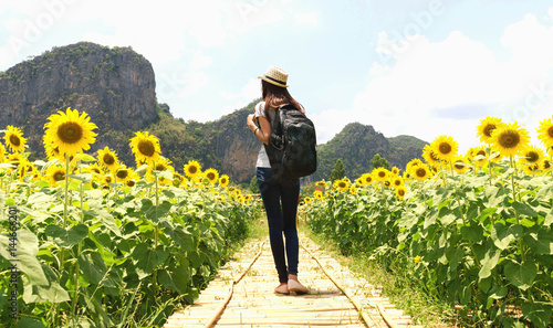 Traveling woman with backpack and straw hat looking sunflower in field