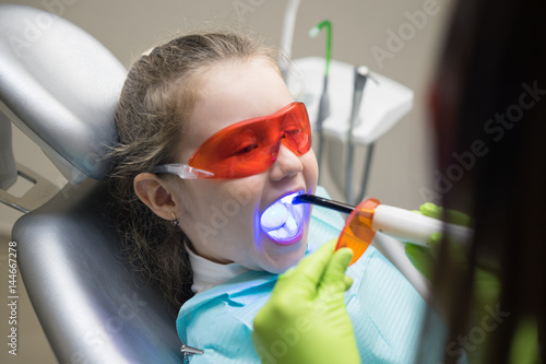 close up view of small girl patient at the dentist. Doctor is making dental fillings with ultraviolet light. Girl is wearing protective glasses photo