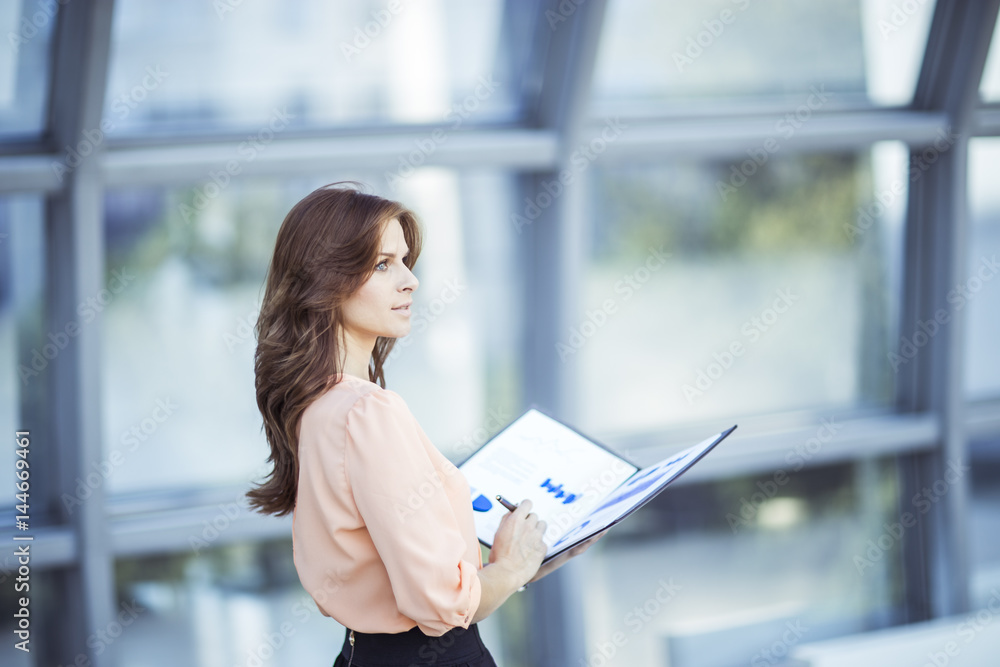 Fototapeta premium successful business woman with financial documents standing near a large window in a modern office
