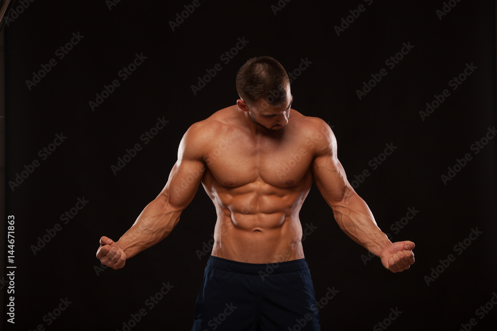 Fototapeta premium Strong Athletic Man Fitness Model Torso showing six pack abs. isolated on black background with copyspace is looking at himself