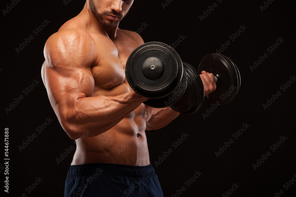Muscular handsome man is training with dumbbells in gym. isolated on black background with copyspace
