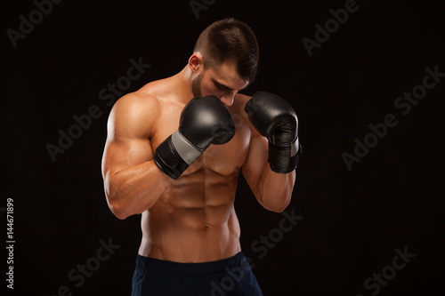 Muscular young man with perfect Torso with six pack abs, in boxing gloves is showing the different movements and strikes isolated on black background with copyspace