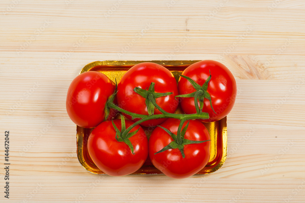 Five fresh red tomatoes with green stem in the tray , isolated on the background Five fresh red tomatoes with green stem in the tray , isolated on the background