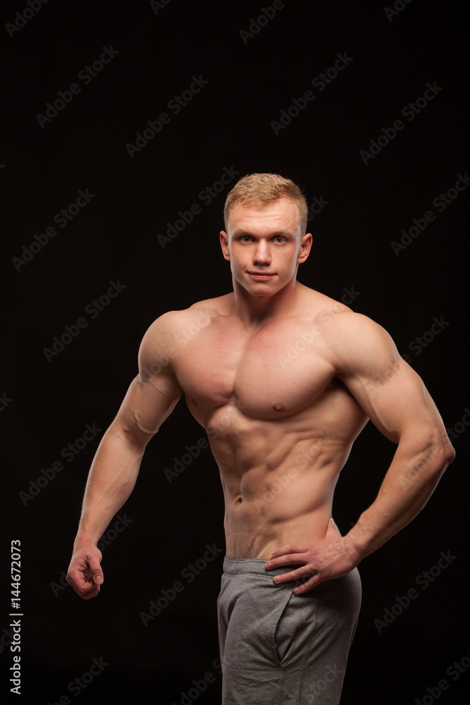 Athletic handsome man fitness-model showing six pack abs and oblique abdominal muscles. isolated on black background with copyspace